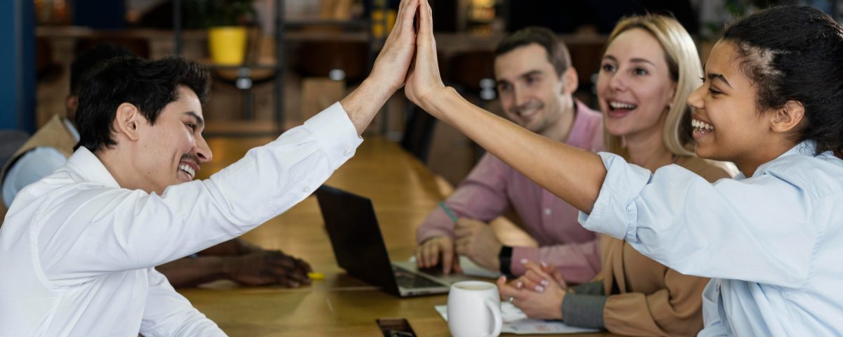 Vista lateral de personas chocando los cinco durante una reunión de oficina