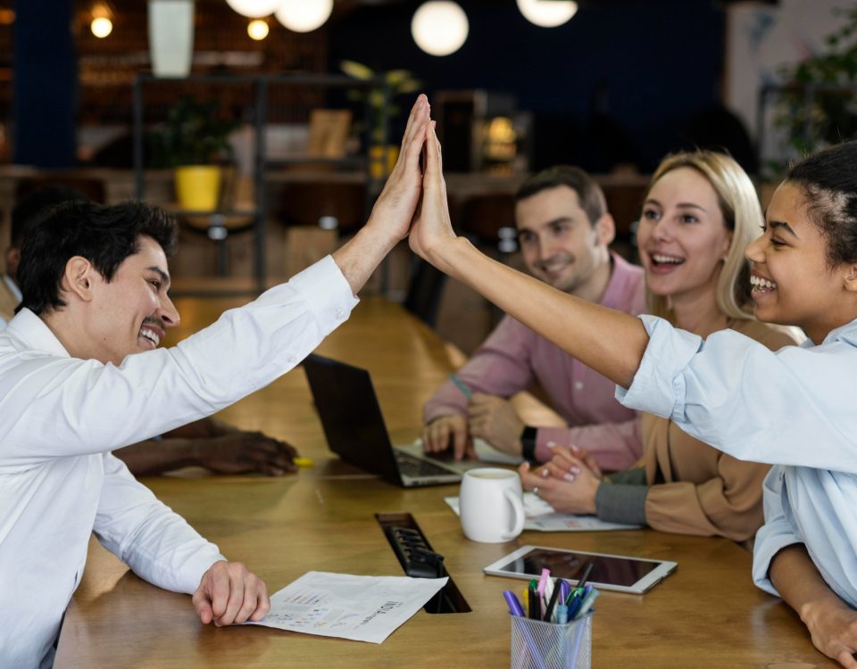Vista lateral de personas chocando los cinco durante una reunión de oficina